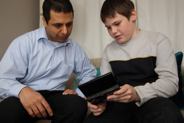 A 10 to 11-year old boy talking to an adult and showing him, what looks like a video game, on a mobile device