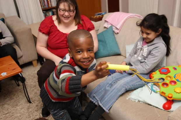 Foster carer plays with a young girl and boy who are smiling and look happy