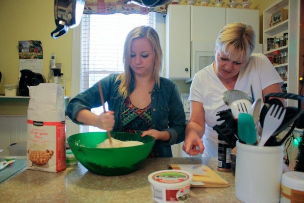 A teenage girl is cooking, helped by a support worker