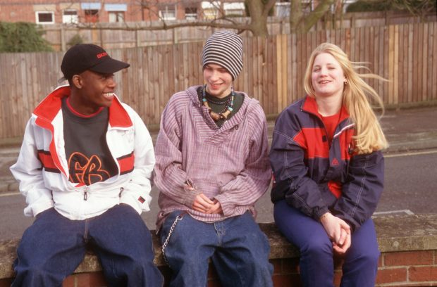 Three happy teenagers sat on a wall smiling and laughing