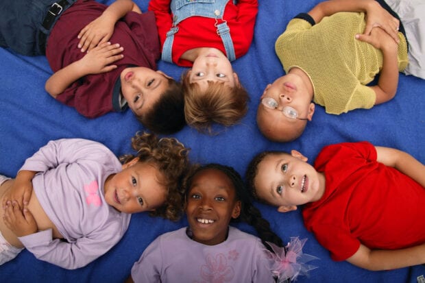 Multiracial group of kids young lying down on ground and looking upwards,