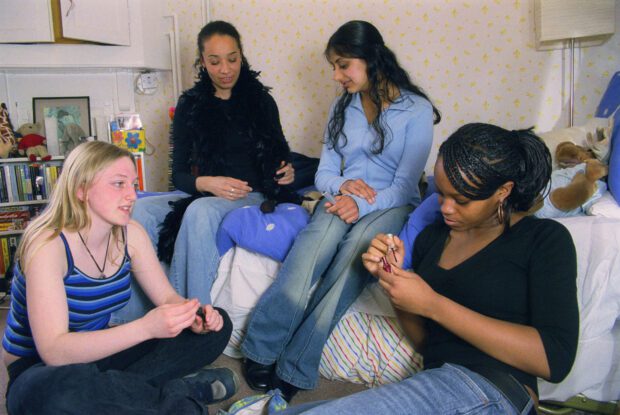 Group of teenage girls sitting together in bedroom painting nails and chatting,