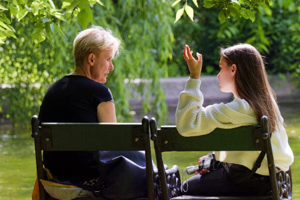 Older woman talking to young girl, sat on garden chairs outdoors