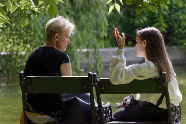 Young person and adult talking on a park bench