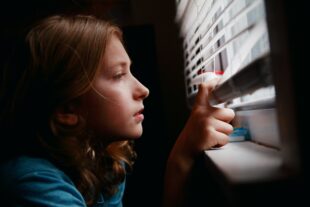 A girl looking out of a window through a set of blinds