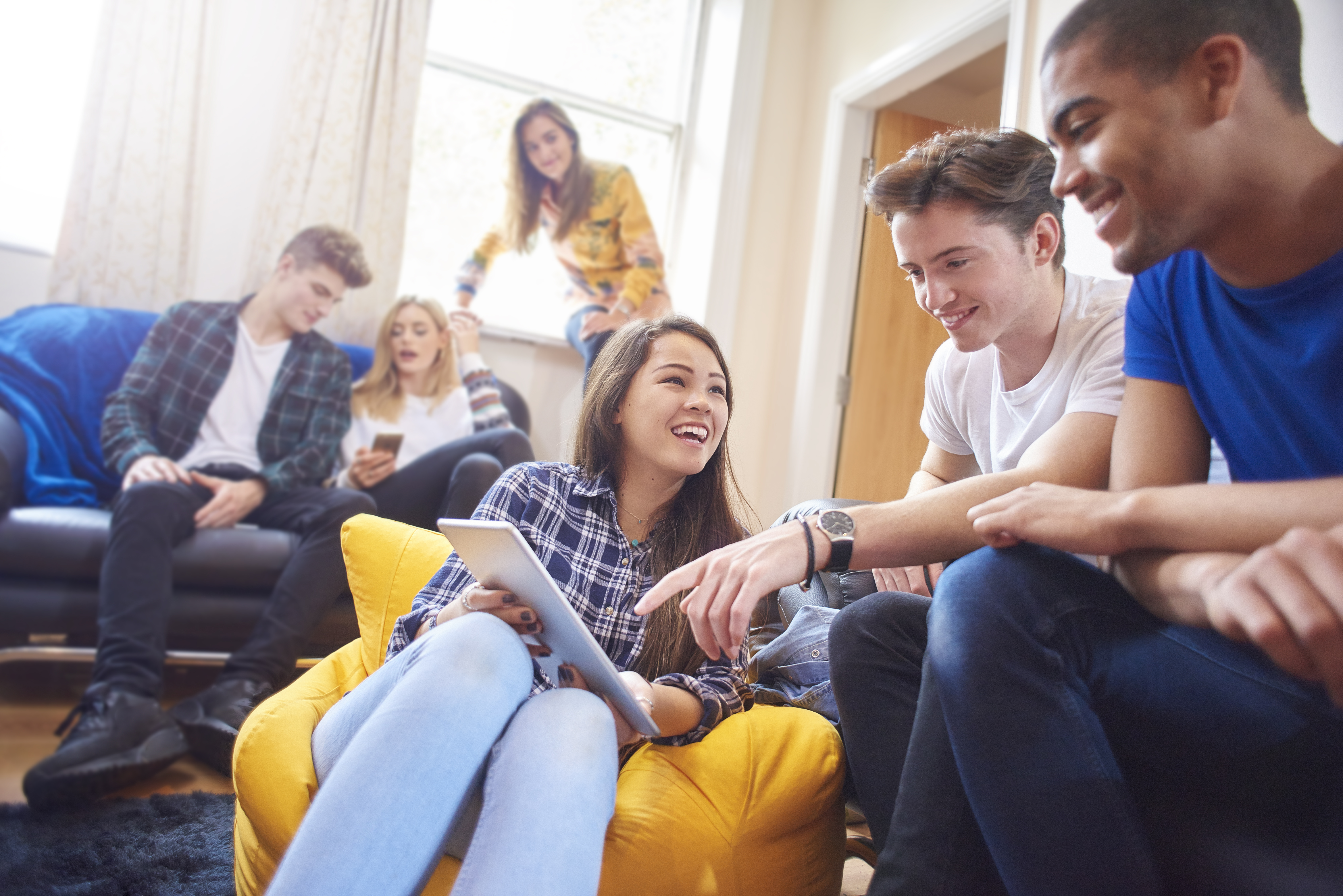 Six young students sit, chatting and socialising with mobile phones and digital tablets.