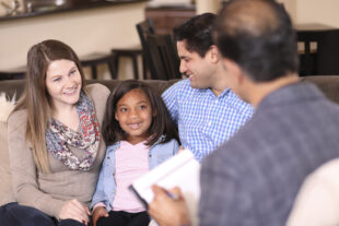 A woman and two men sitting with a young child, smiling and talking. 