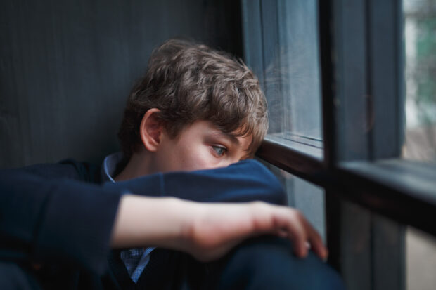 A teenage boy sitting by a window.